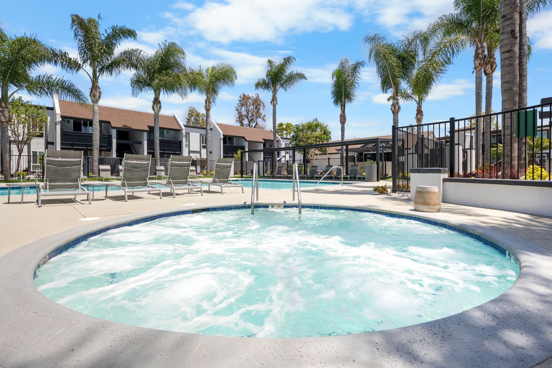 A hot tub is in the middle of a swimming pool surrounded by palm trees.
