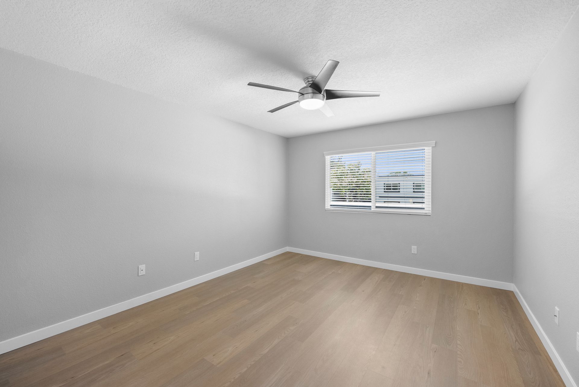 An empty bedroom with a ceiling fan and two windows.