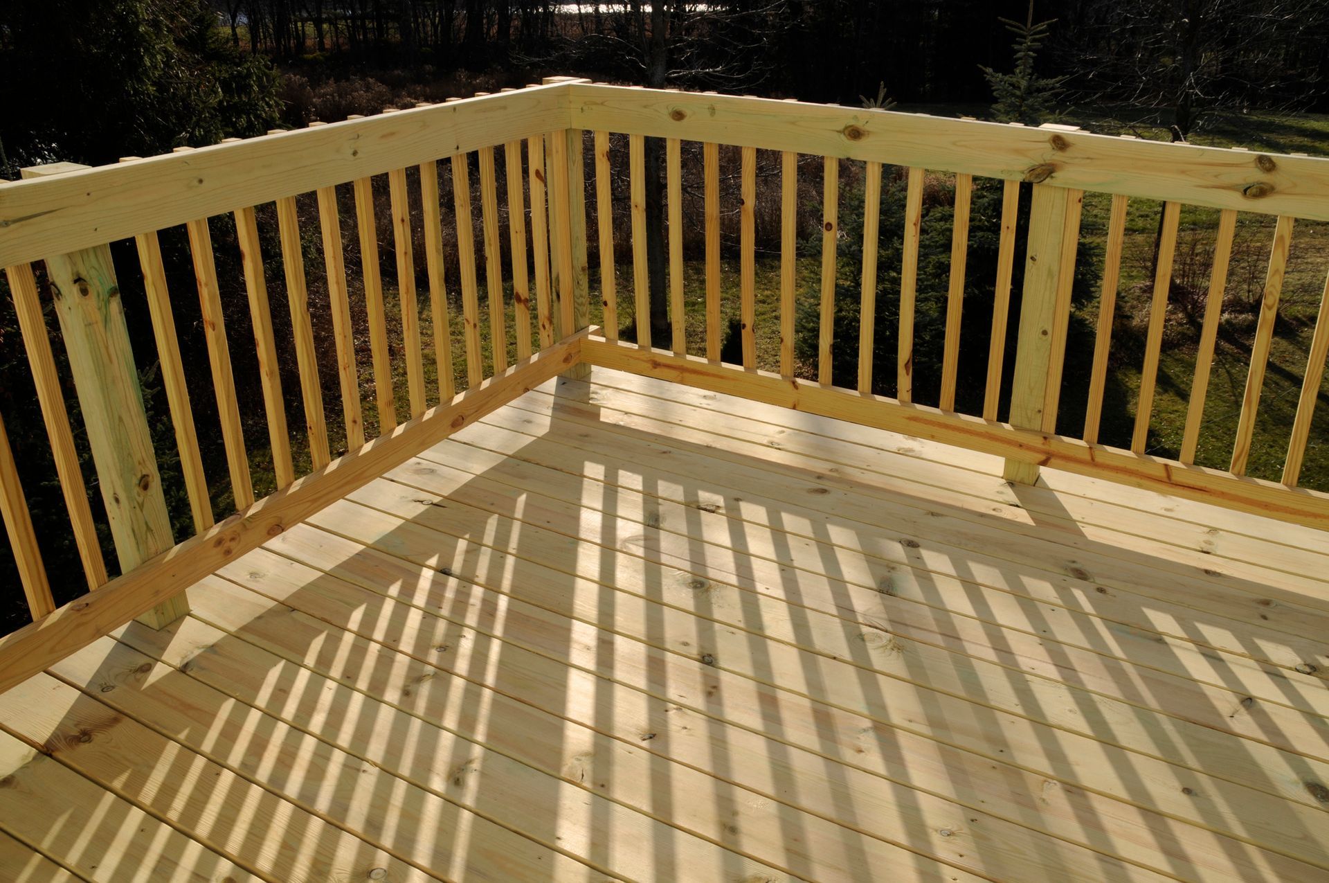 A wooden deck with a railing and shadows on it