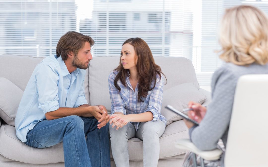 A man and a woman are sitting on a couch talking to a woman.