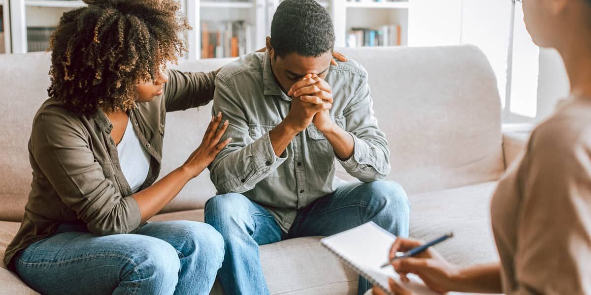 A man and a woman are sitting on a couch talking to a therapist.