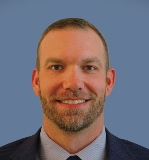 Smiling man in a suit and tie against a blue background.