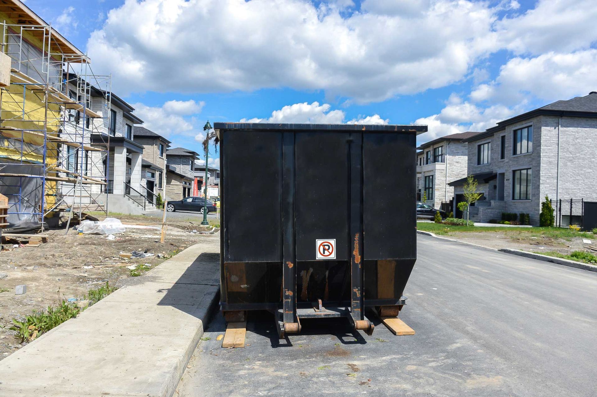 Large waste receptacles filled with construction debris near building site under clear blue sky.
