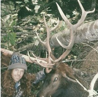 A man smiling while petting an elk.