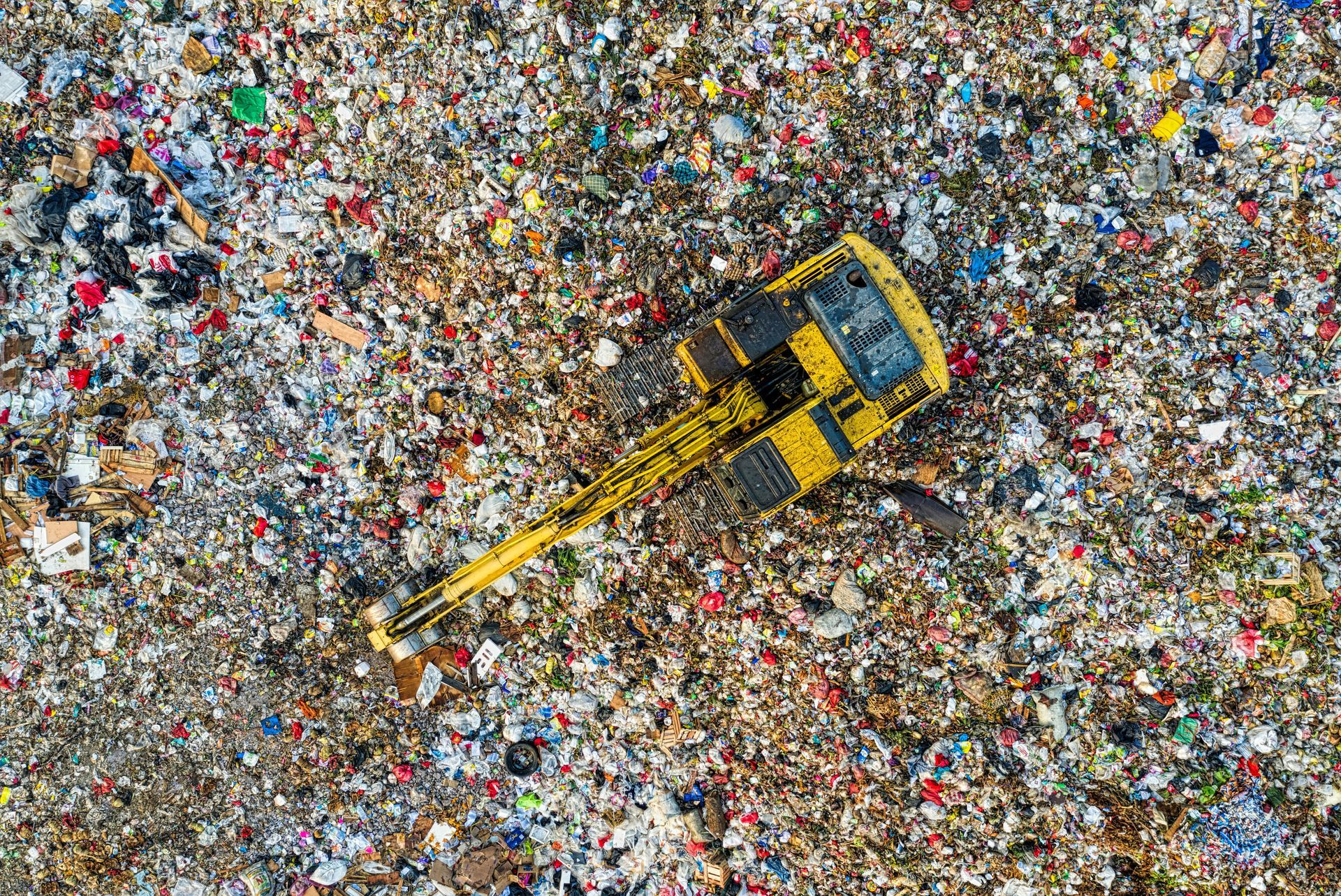 A yellow excavator is sitting on top of a pile of trash Pinellas Family Junk Removal.