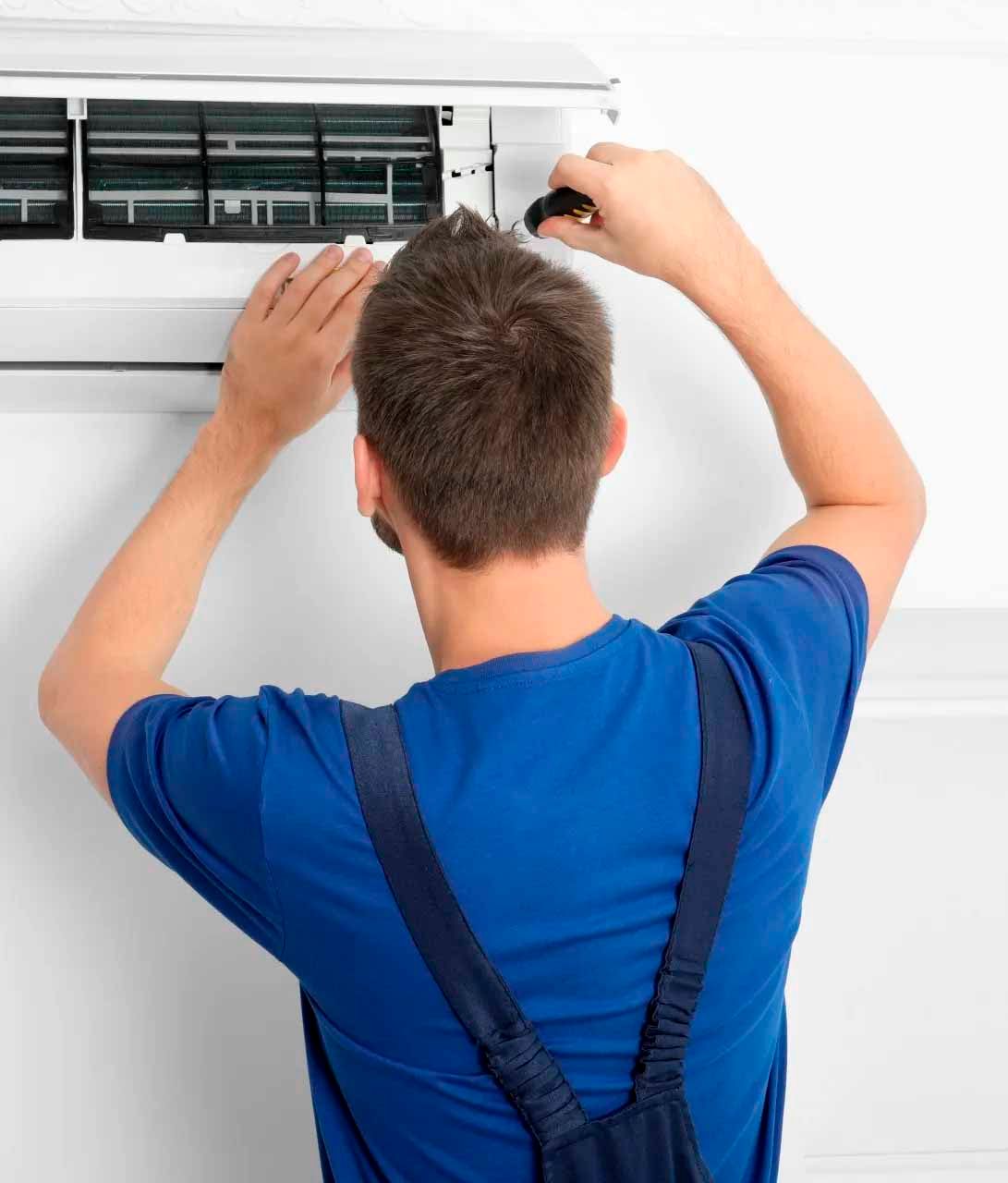 Un homme en chemise bleue travaille sur un climatiseur