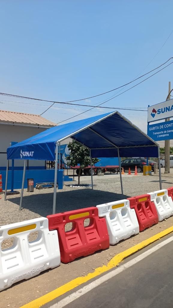 Una carpa azul está colocada al costado de la carretera al lado de una fila de barreras de plástico.