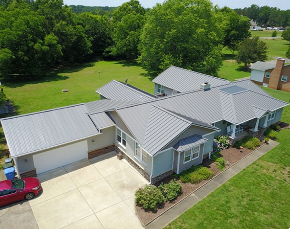 Aerial view of a gray-roofed suburban house with a driveway, red car, and green trees nearby
