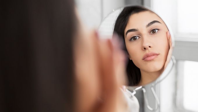 girl touching her face while looking in small round mirror
