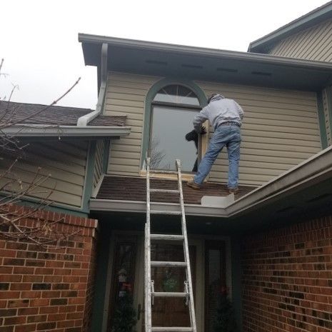 A Man Is Standing on A Ladder on The Roof of A House - Bellbrook, OH - John Henry Painting LLC