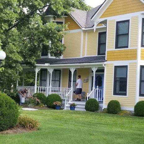 A Man Is Standing on The Porch of A Yellow House - Bellbrook, OH - John Henry Painting LLC