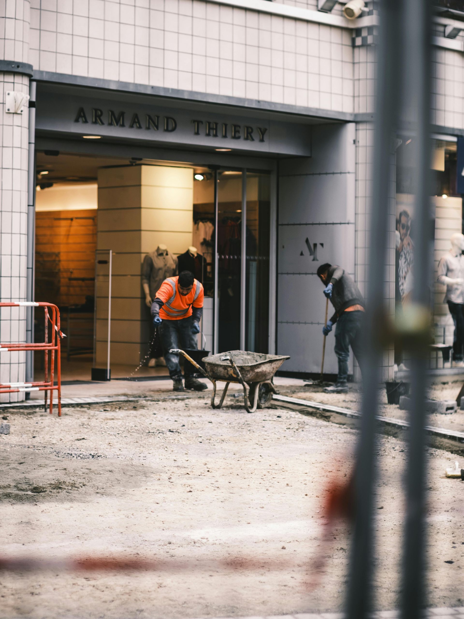Construction workers outside the Armand Thierry store, with a wheelbarrow and tools. Grayscale.