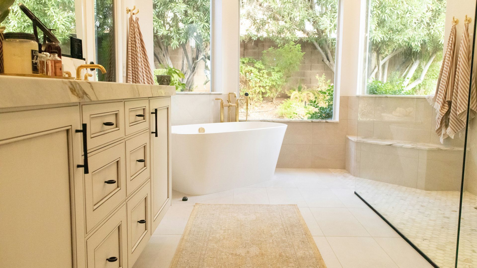 A cream white bathroom with large windows, a freestanding bathtub, and a stone step.