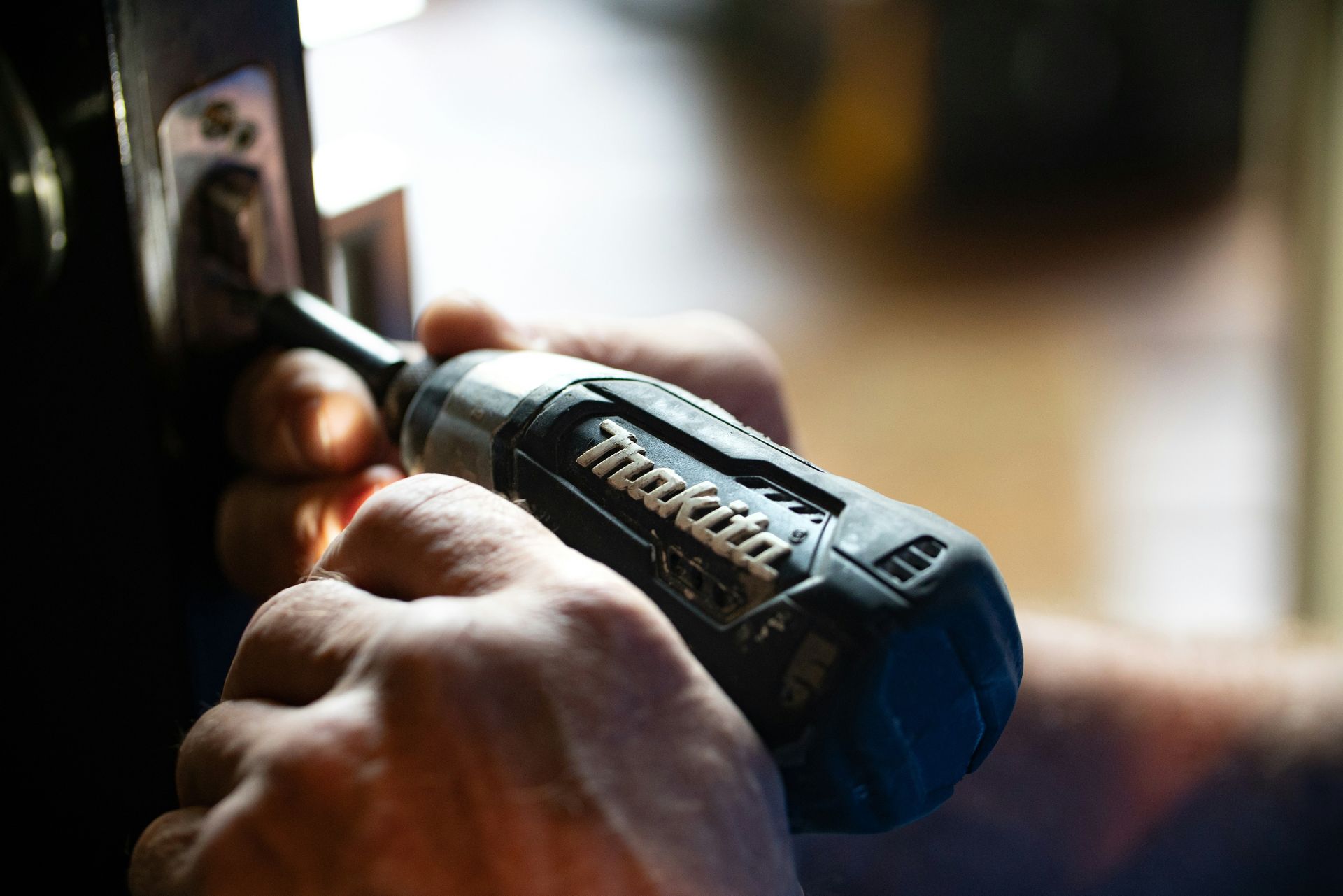 A professional repair man drilling on a hinge.