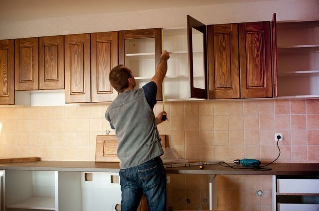 A man is measuring a cabinet in a kitchen with a tape measure.