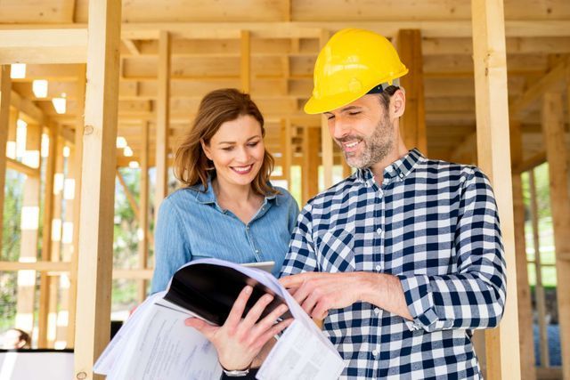 A man and a woman are looking at a blueprint at a construction site.
