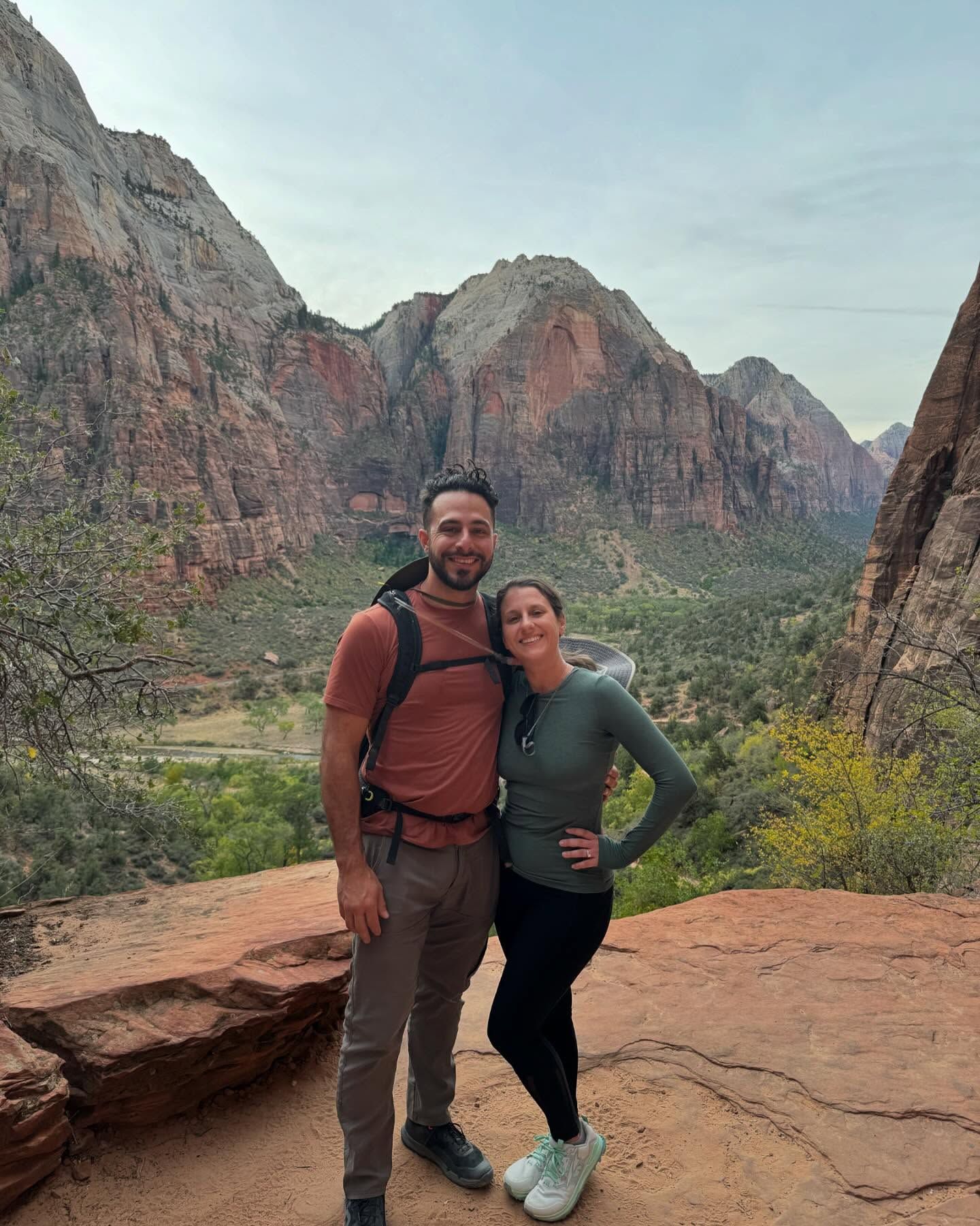 Couple poses for photo on a mountain trail with canyon view. 