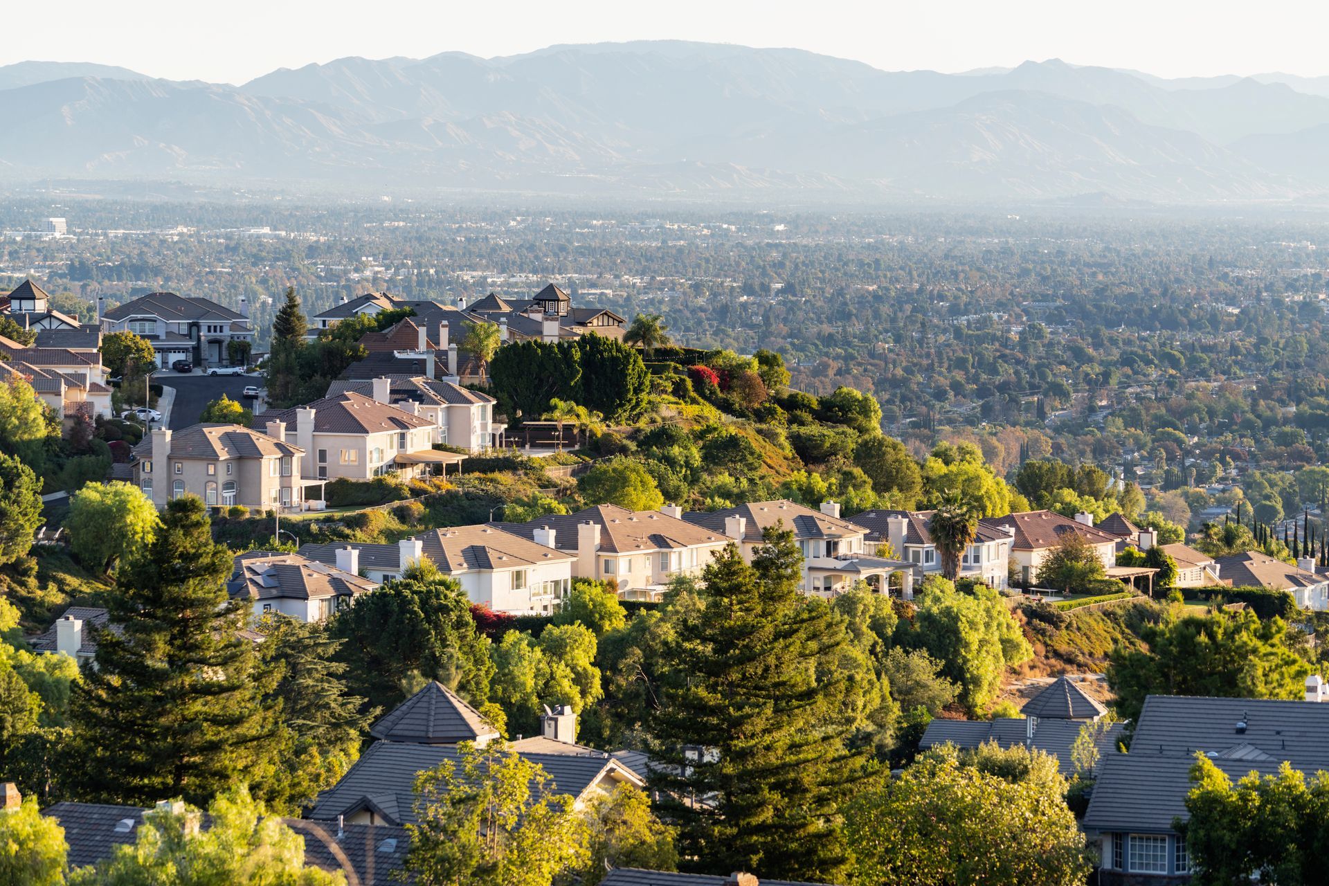 Houses on a hillside overlooking a sprawling city, with mountains in the background.