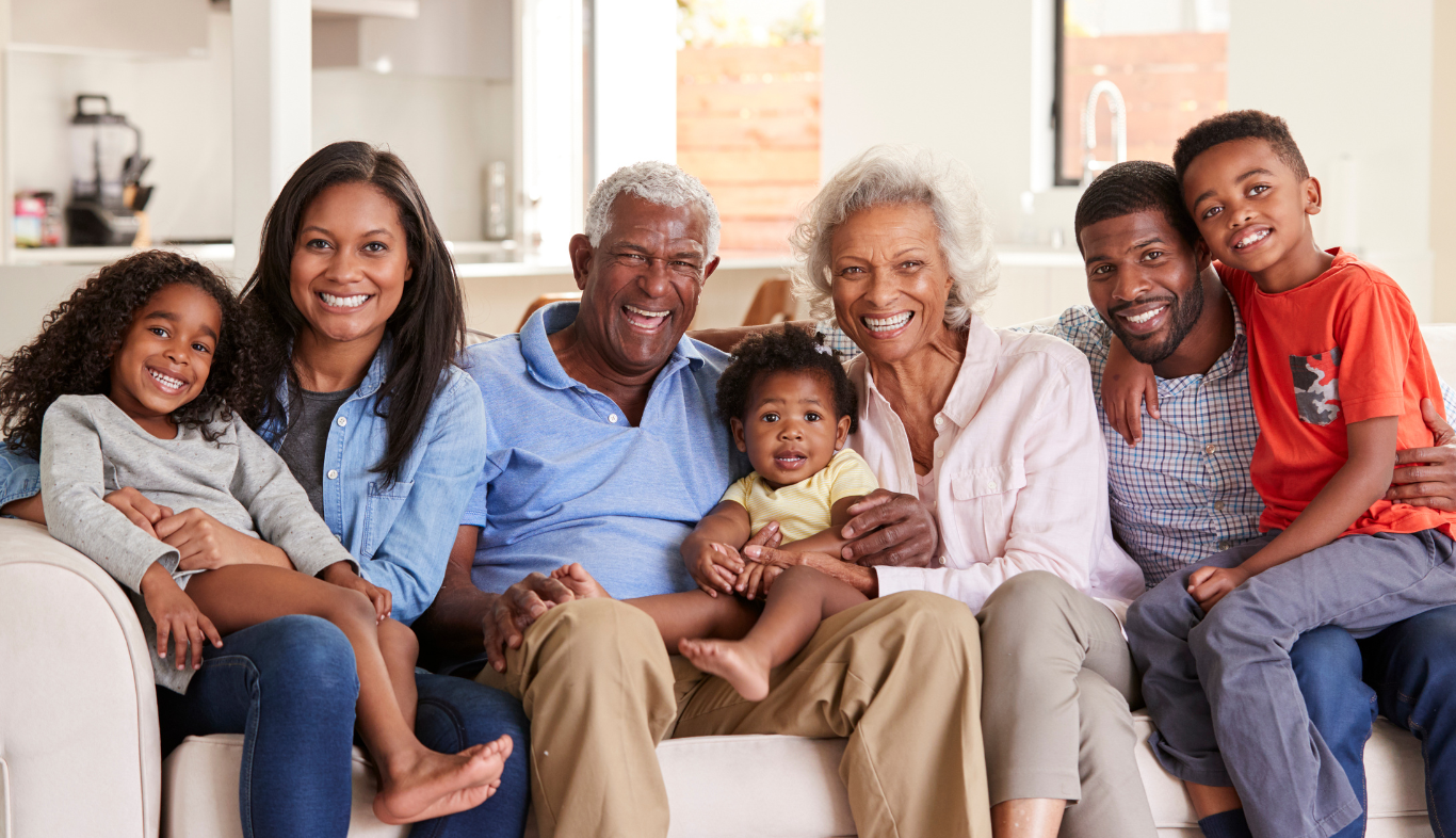 Multigenerational Black family smiling on a couch in a well-lit living room.