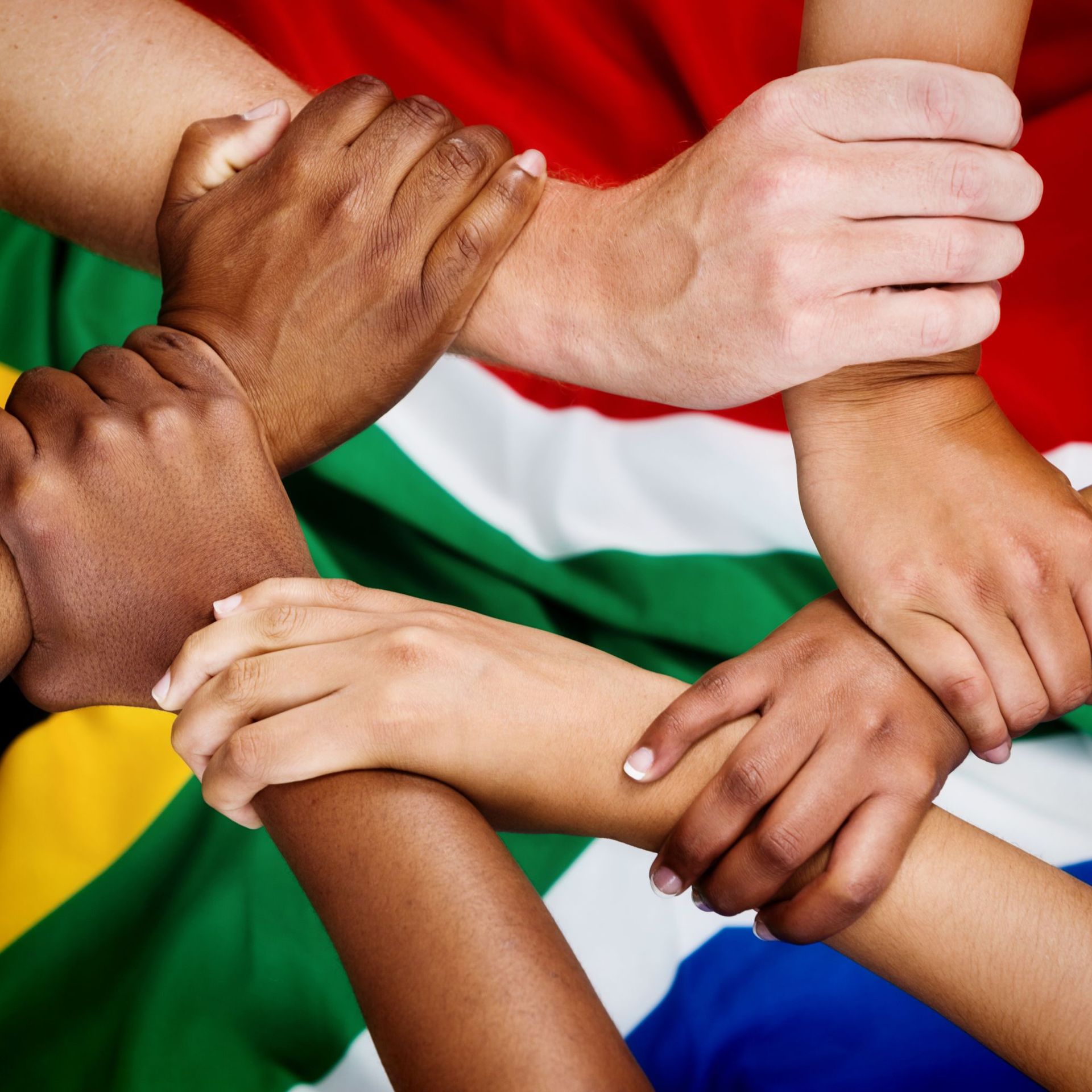 Hands of various skin tones clasped together, over the South African flag, symbolizing unity.