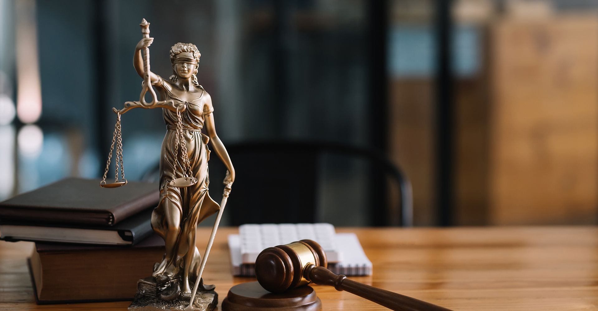 A statue of justice is sitting on a wooden table next to a wooden gavel.