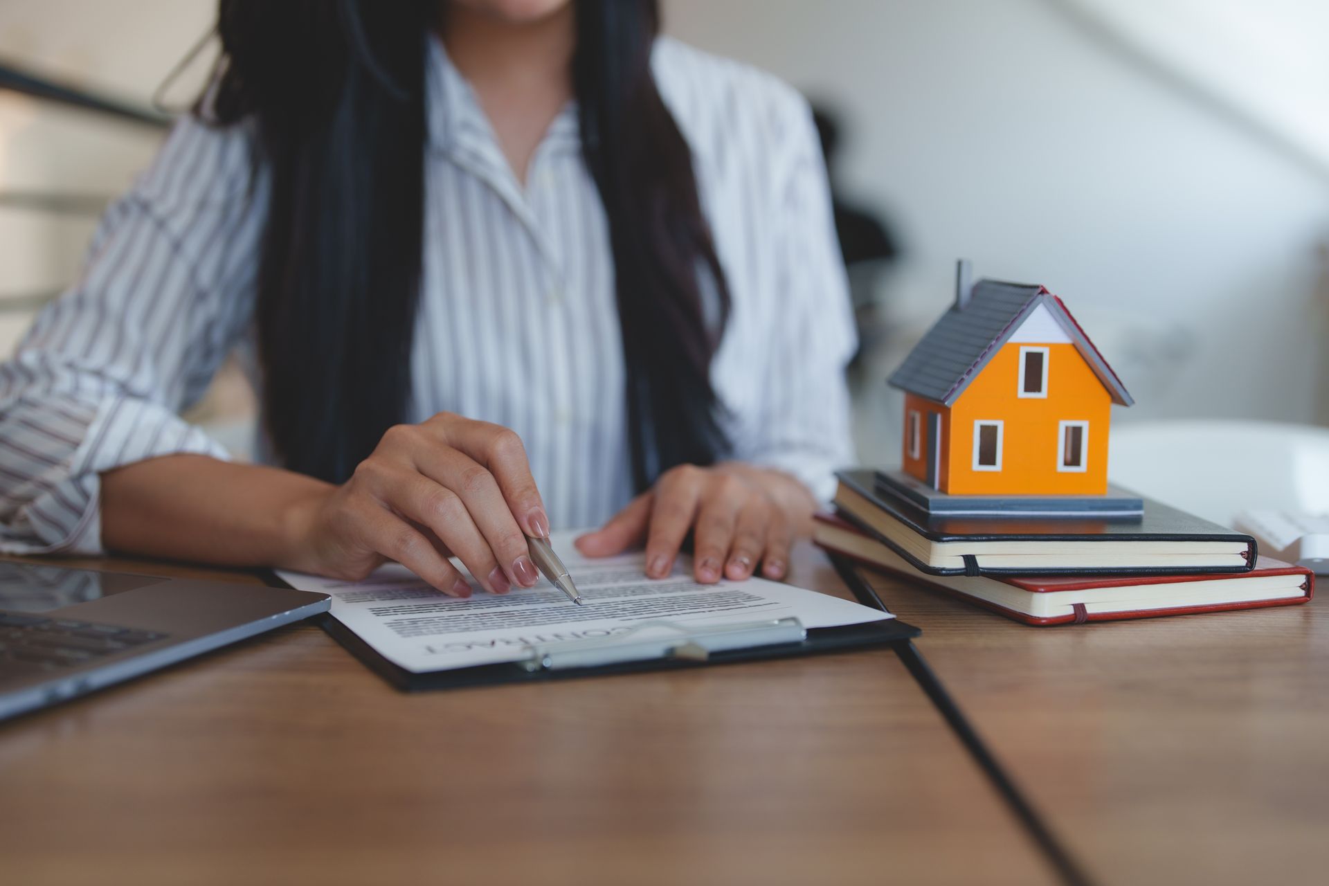 Woman reviewing documents with a model house on books at a desk.