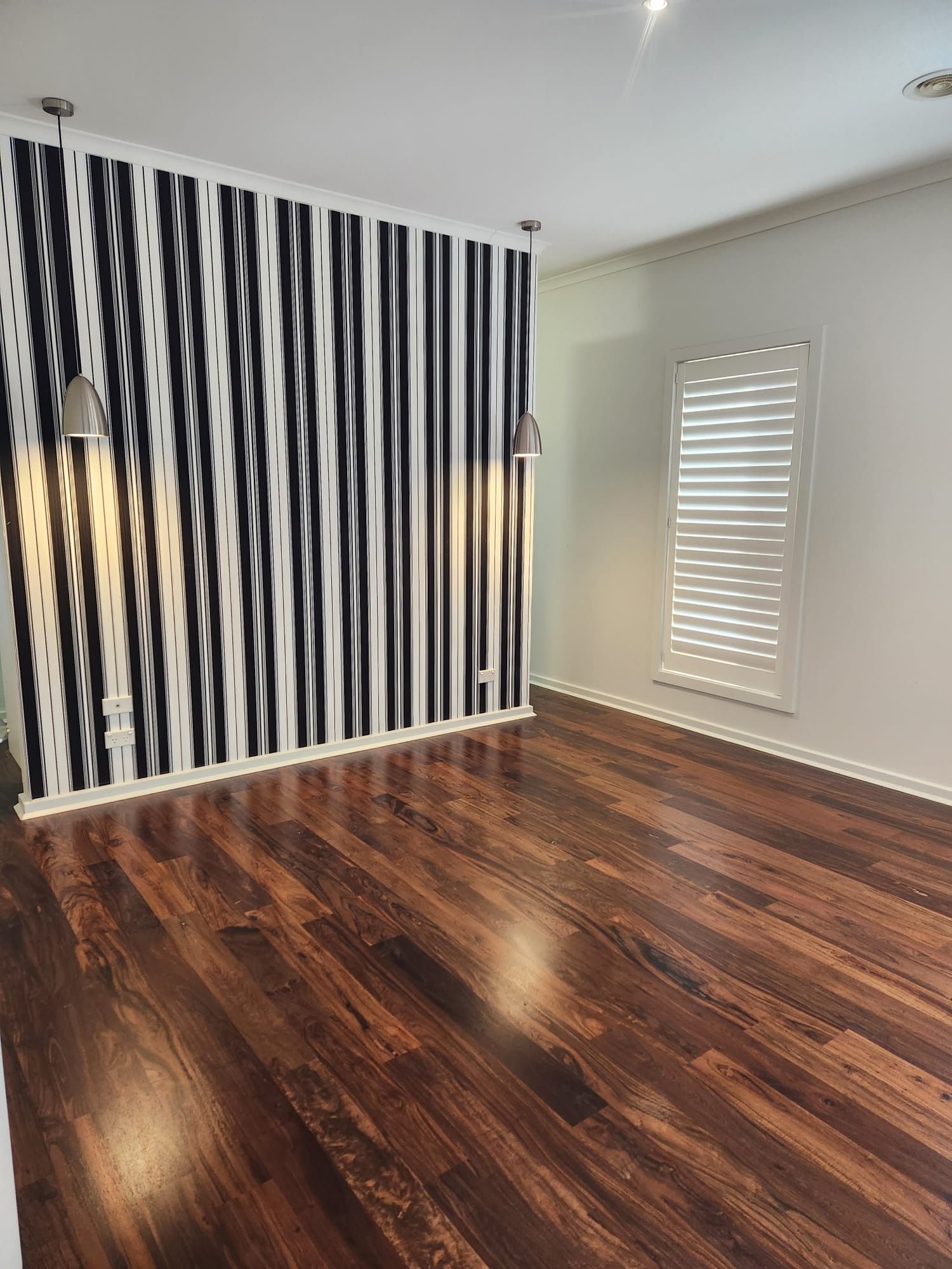 Empty room with dark wood floors, black-and-white striped accent wall, and a window with blinds.