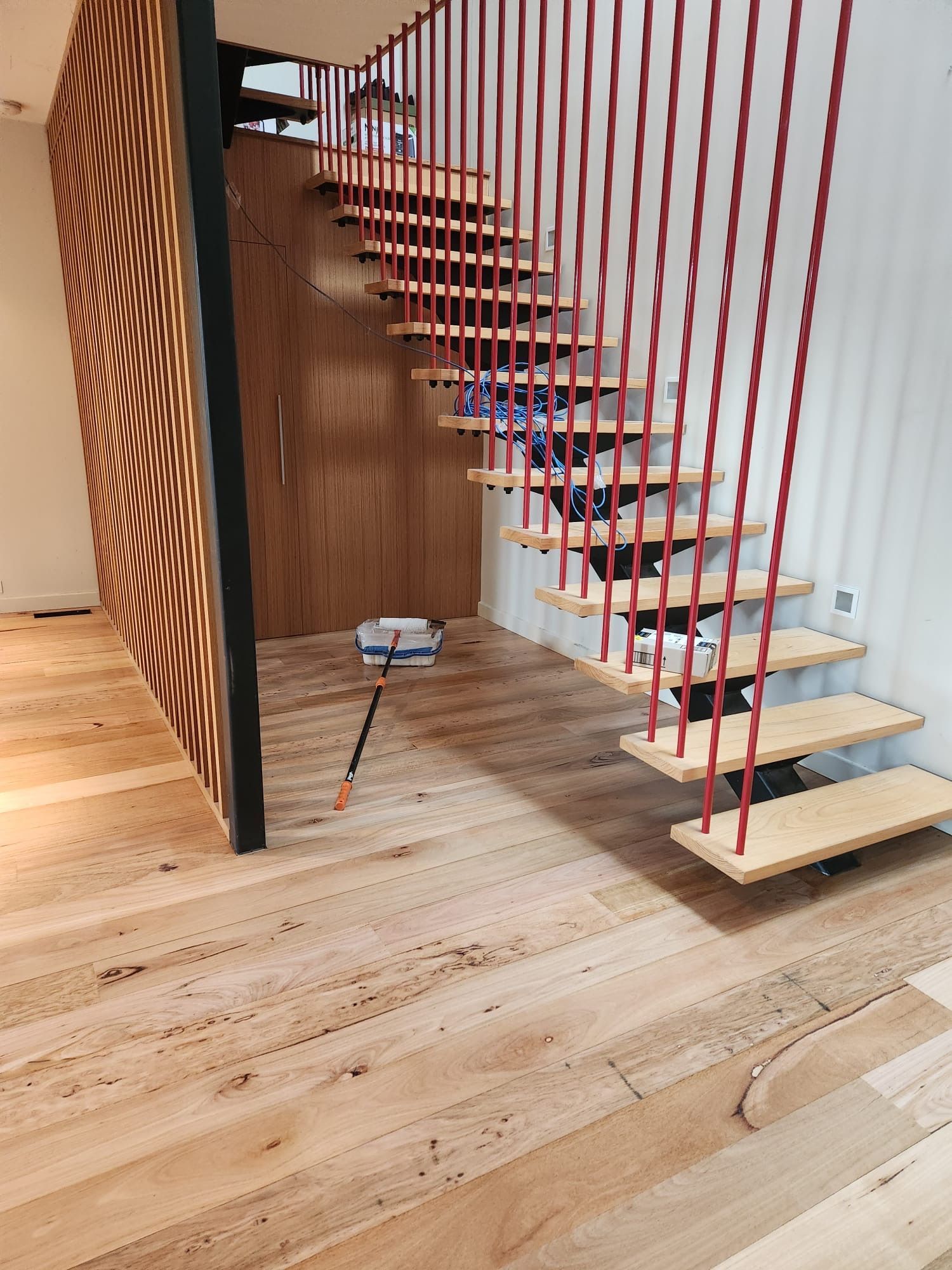 Modern wooden staircase with open treads, red vertical cables, and light wood flooring in a minimalist interior