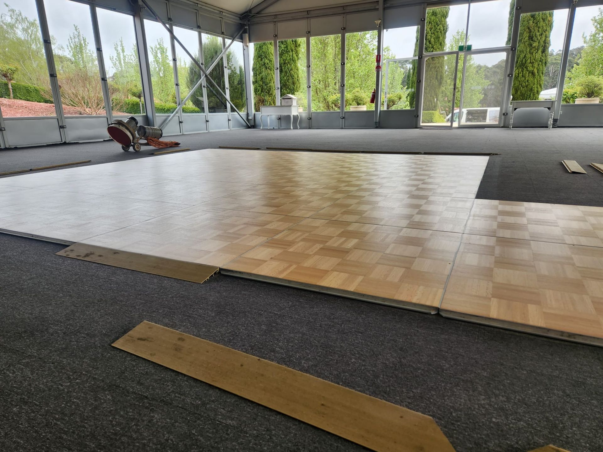 Empty indoor pavilion with wooden parquet dance floor and dark carpet, open sides overlooking greenery