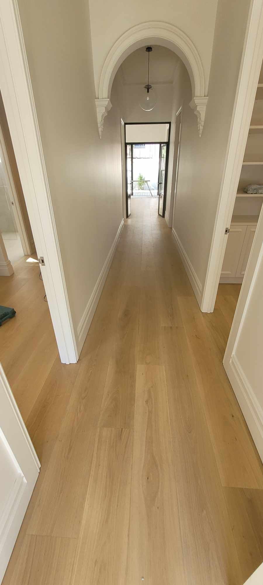 Narrow hallway with arched ceiling and wooden floorboards, leading to a door opening to natural light.