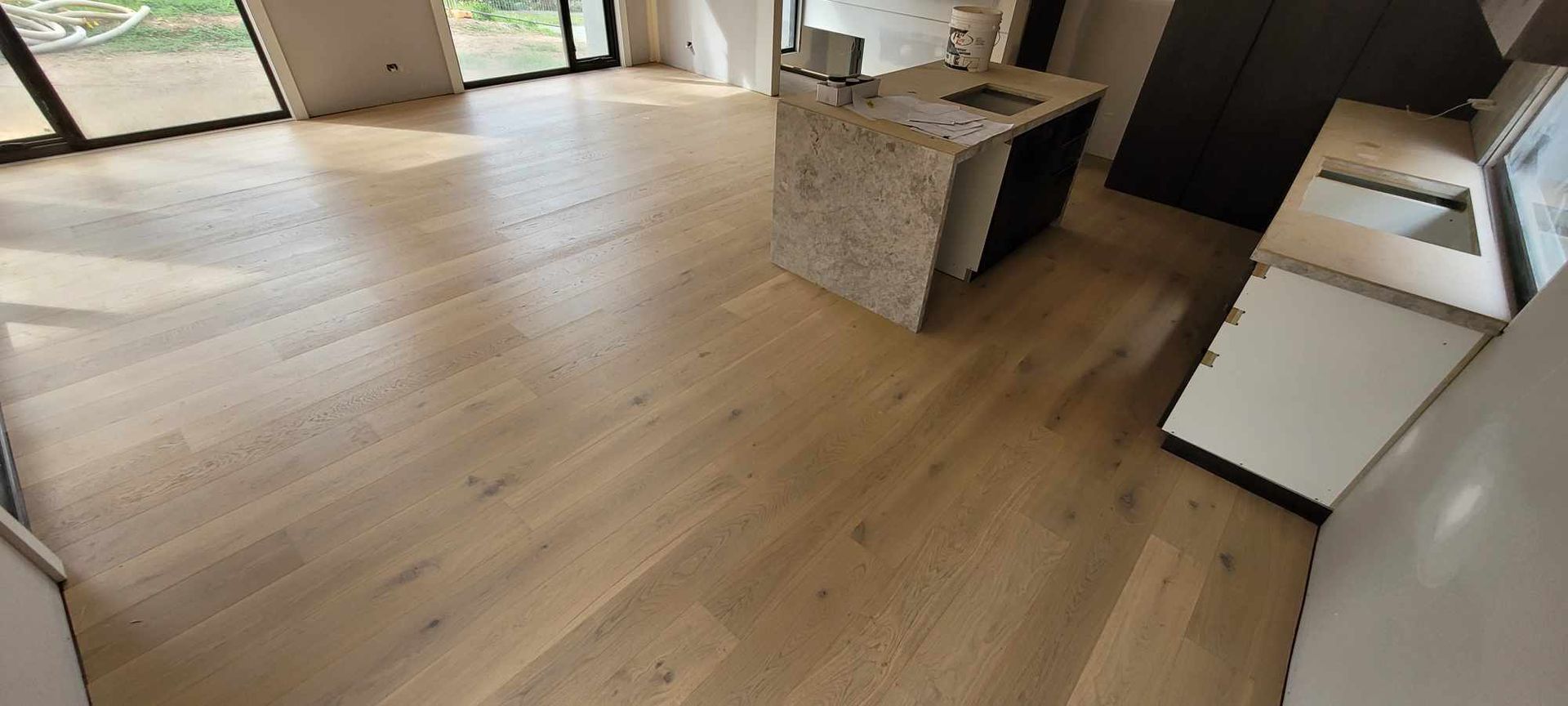 Light wood flooring in a kitchen with a stone countertop island and white cabinets.