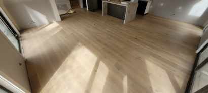 Wooden flooring in a room with a countertop and natural light casting shadows.