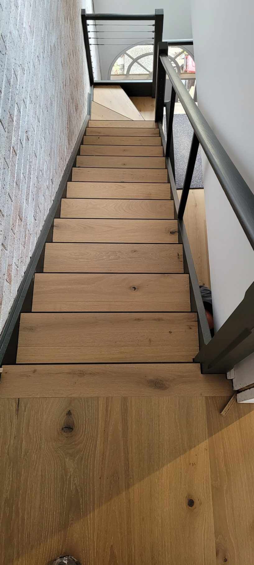 Wooden staircase with black metal railing in a narrow space, leading up to a window.