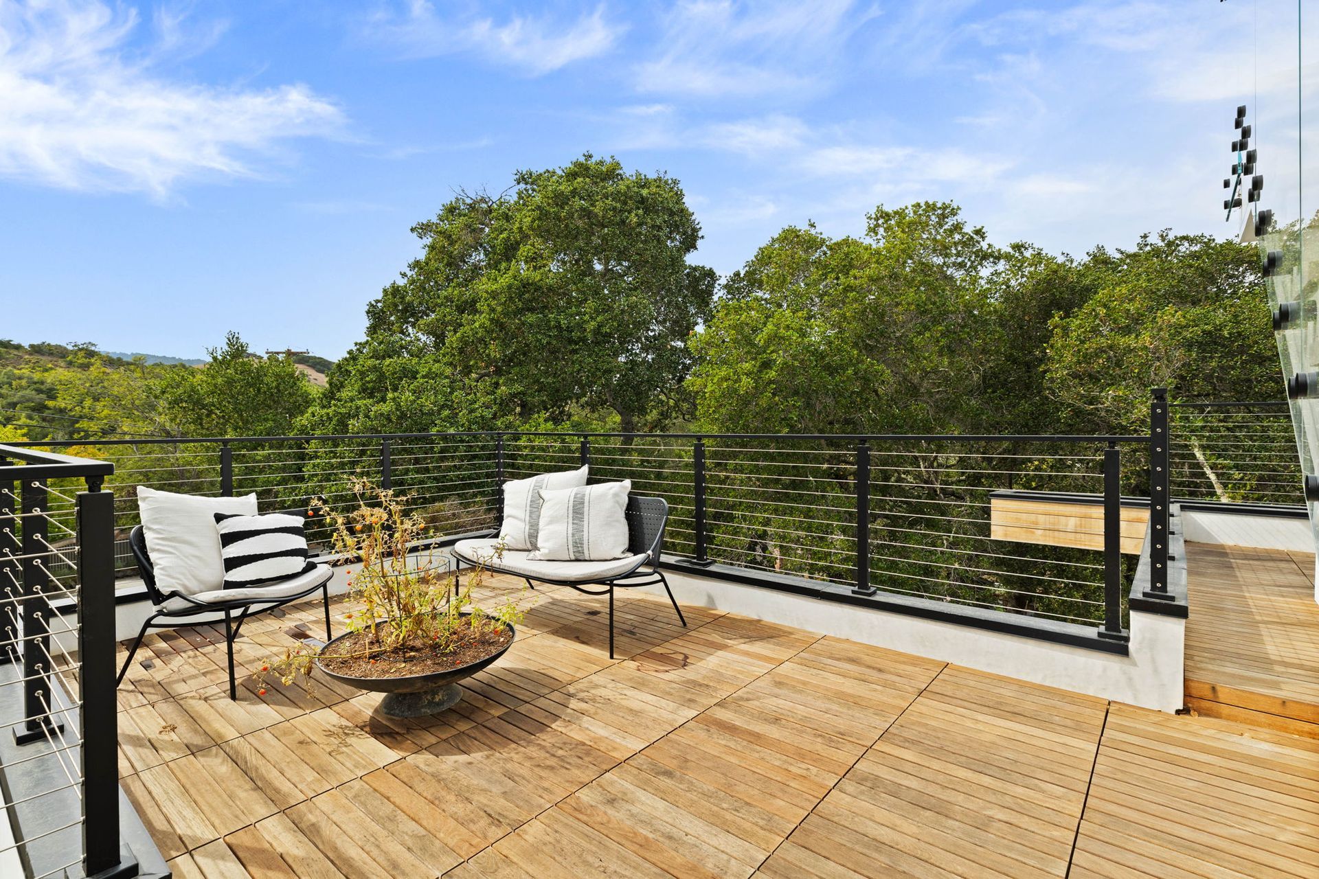 Rooftop deck with seating, overlooking lush trees and a blue sky.