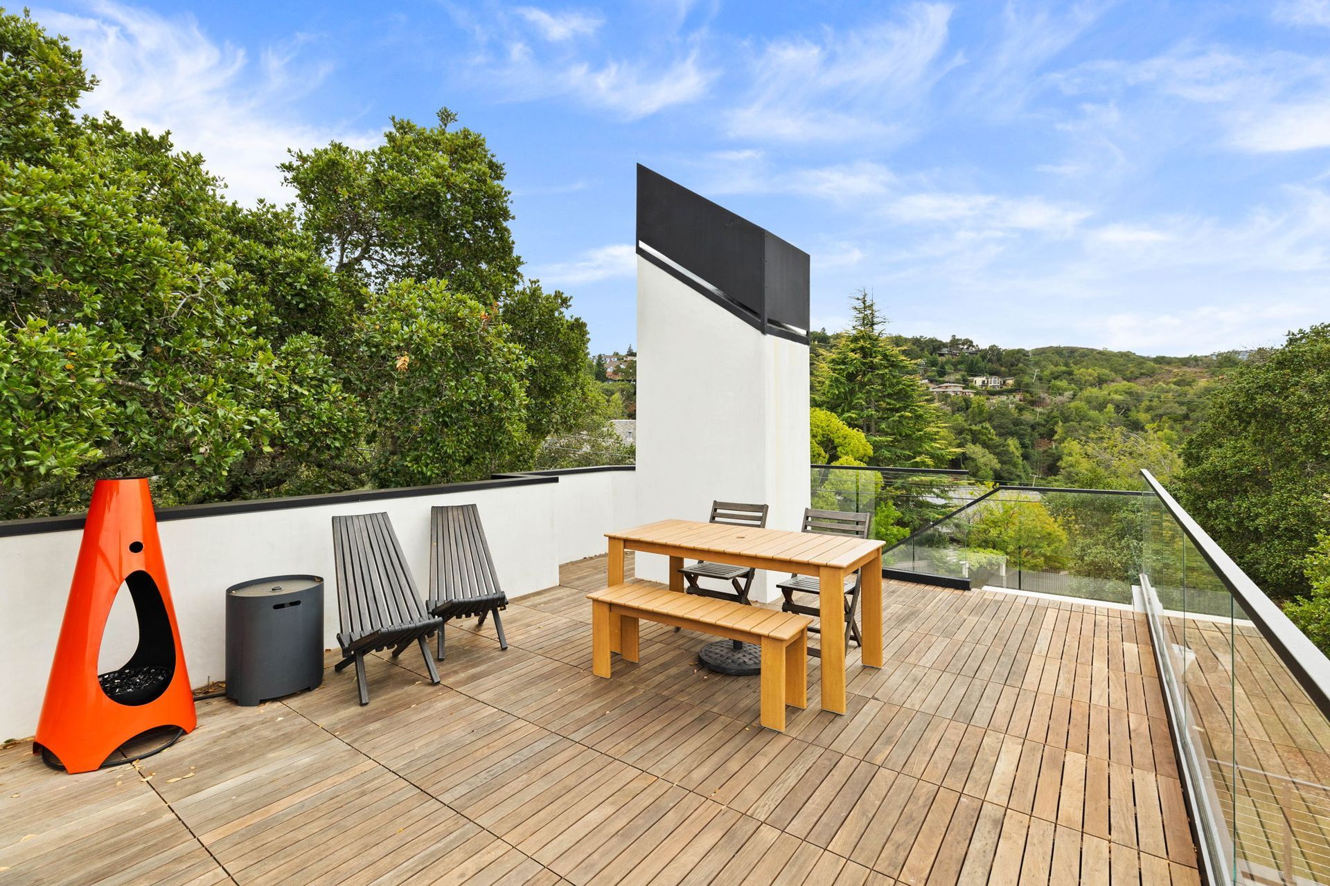 Rooftop deck with wooden furniture, overlooking trees.