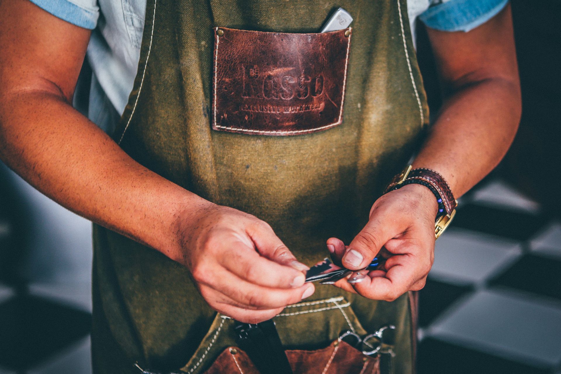A person wearing an apron, holding small metal objects, possibly tools, with hands clasped.