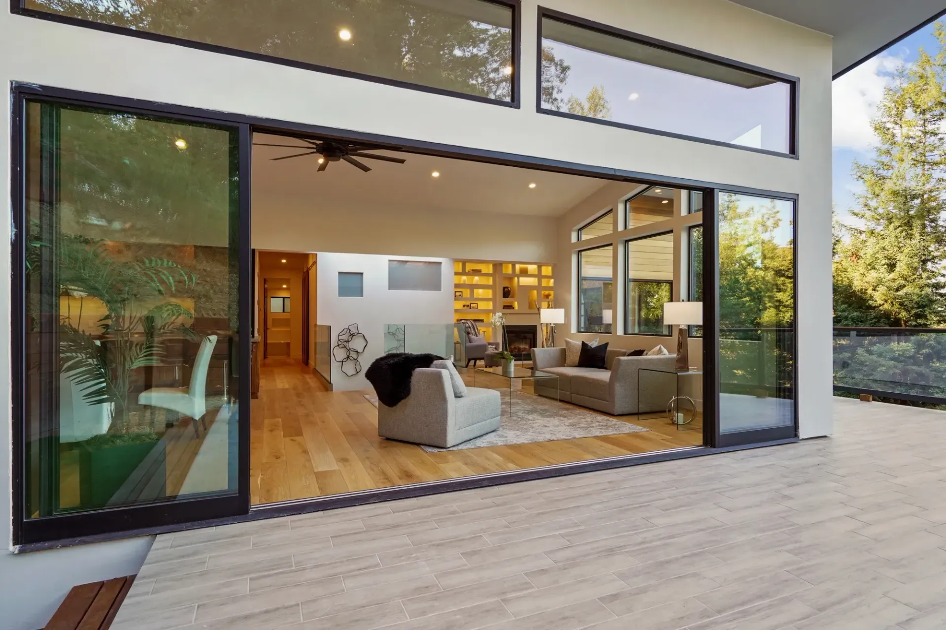 Open glass doors reveal a living room, with wooden floors, facing a wooden deck.