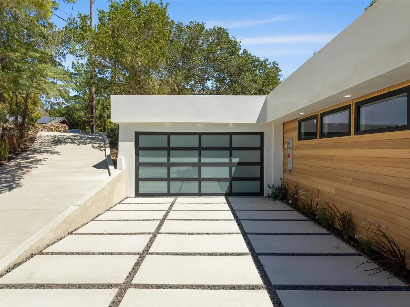 Modern home exterior with a concrete driveway and glass garage door.