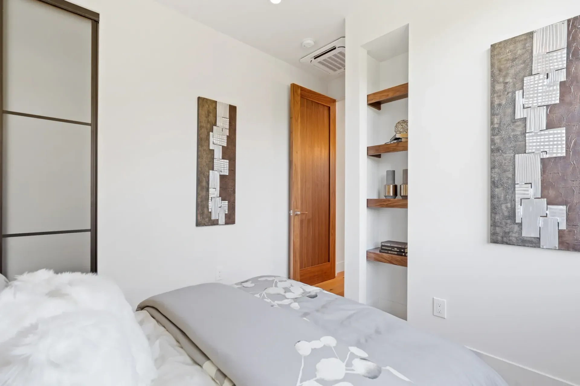 Bedroom with bed, wall art, wooden shelves, and a closed wooden door.