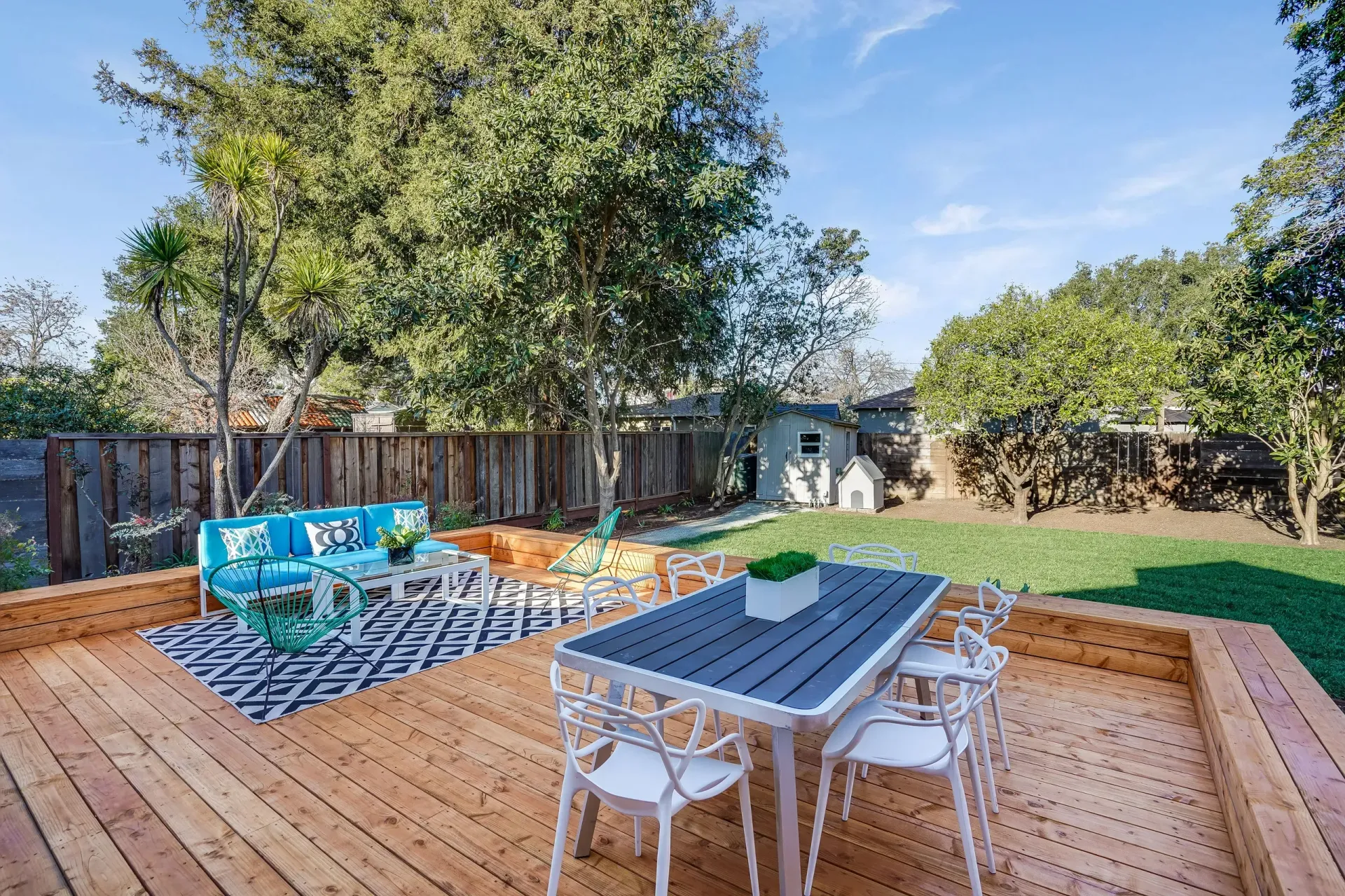 Wooden deck with outdoor furniture, and backyard with lawn and trees.