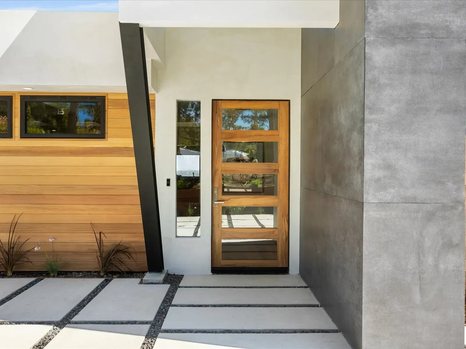 Modern home entrance with wooden door, concrete path, and light wood siding.
