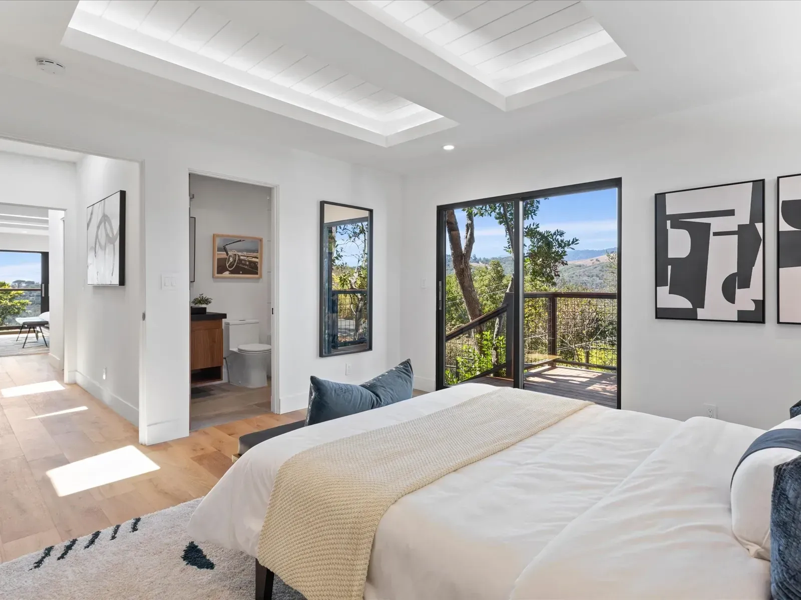 Bedroom with bed, large window overlooking trees, and artwork on wall.