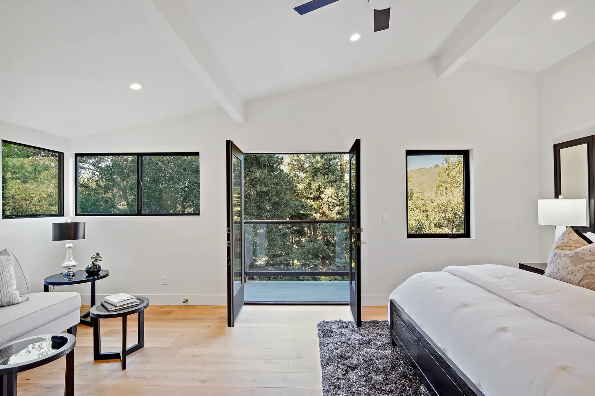 Bedroom with open black doors to outside view, and light wood floors.
