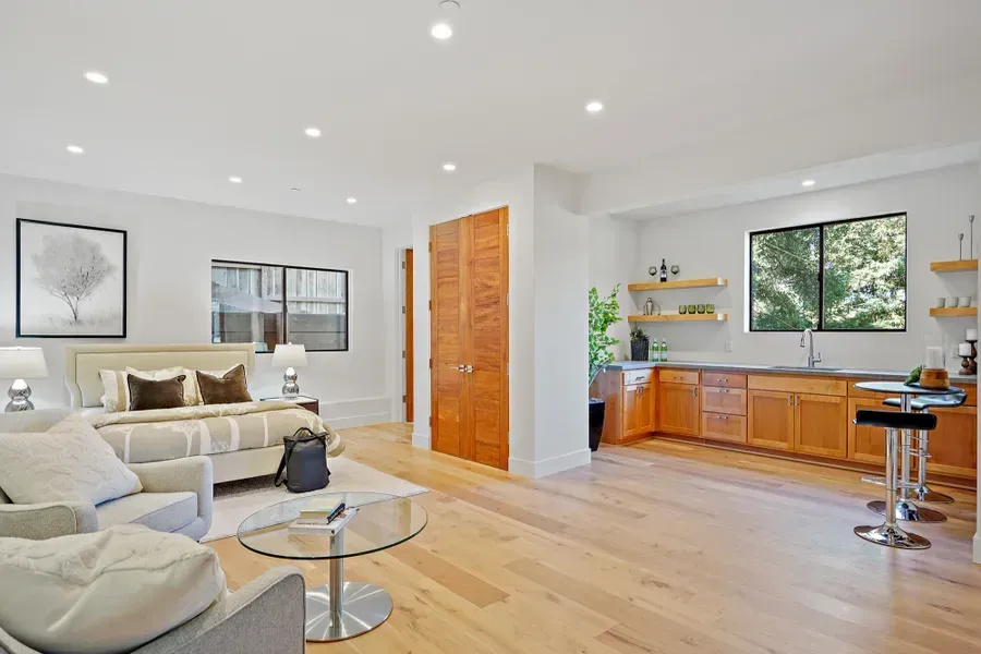 Bright studio apartment with bed, kitchenette, seating, and wooden flooring.