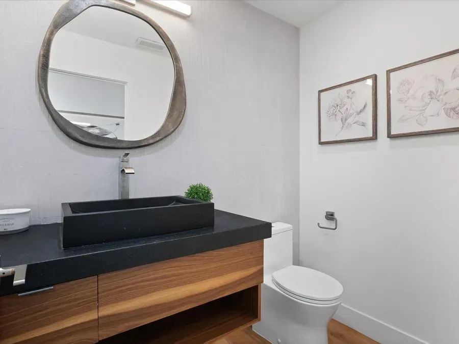 Modern bathroom with wood vanity, black rectangular sink, round mirror, and framed floral prints.