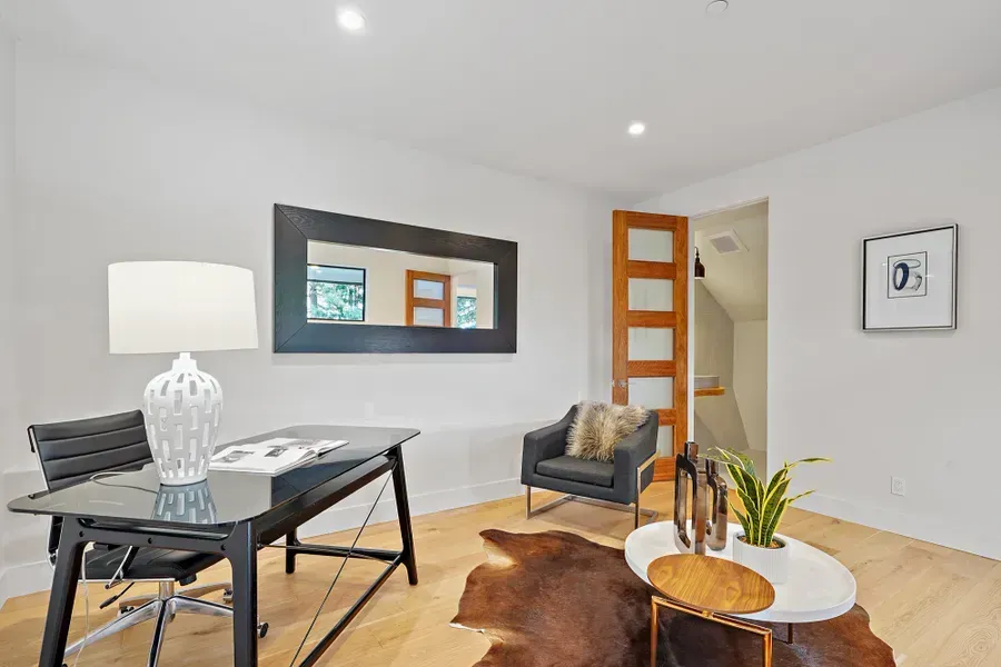 Modern home office with black desk, chair, and large mirror, accented by a cowhide rug and wood floors.