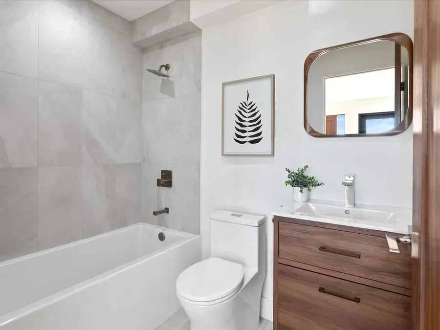 Modern bathroom with white tub, toilet, and vanity with dark wood.