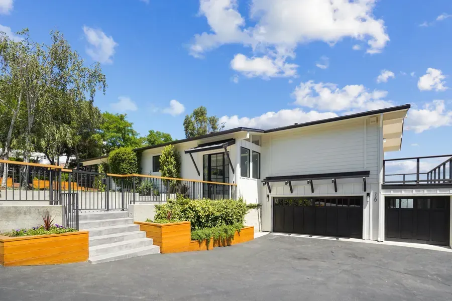 White house with black accents, black garage doors, deck, and concrete steps on a sunny day.
