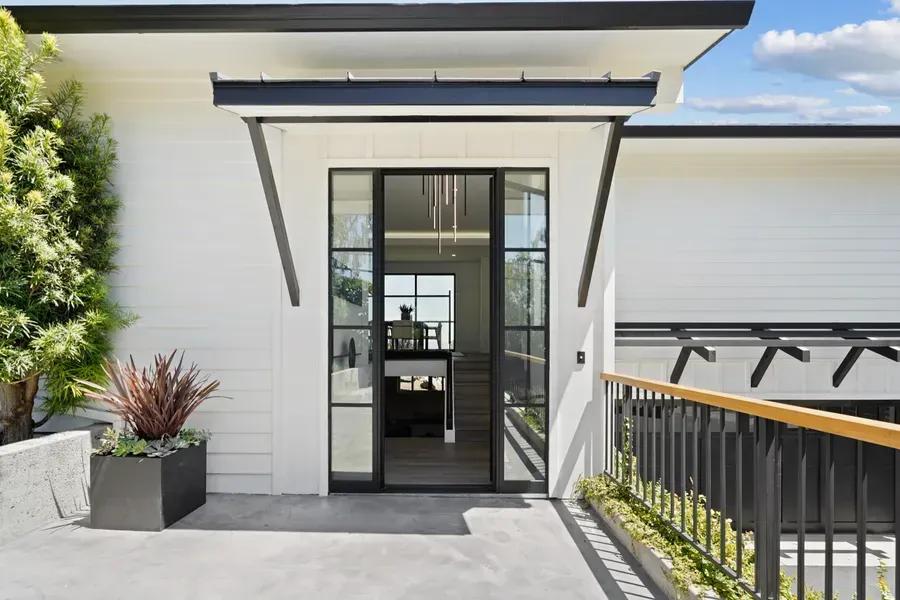Modern home exterior with black-framed glass door, white siding, and a small balcony with a wooden rail.