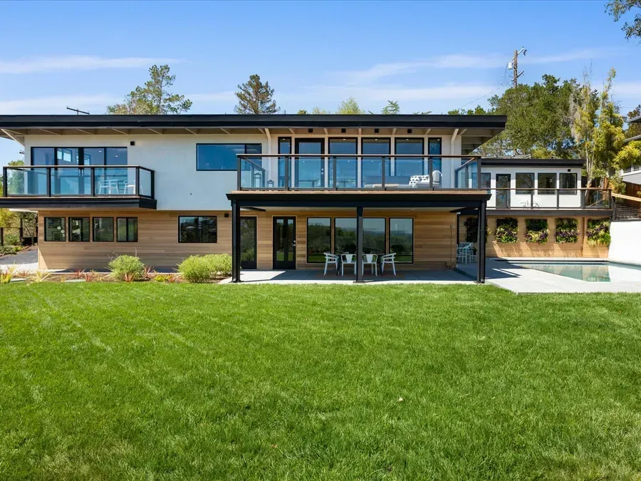 Modern two-story house with black trim, glass balconies, and a green lawn. There's also a pool.